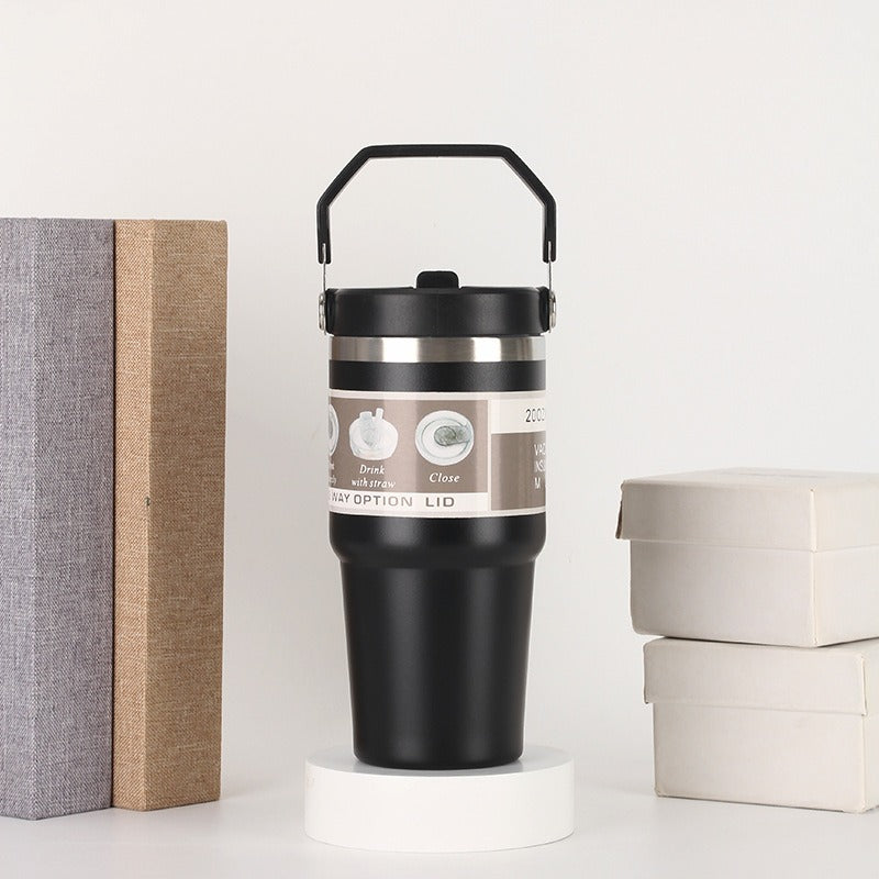 Black stainless steel travel mug with handle, displayed between books and gift boxes, sps street style gift
