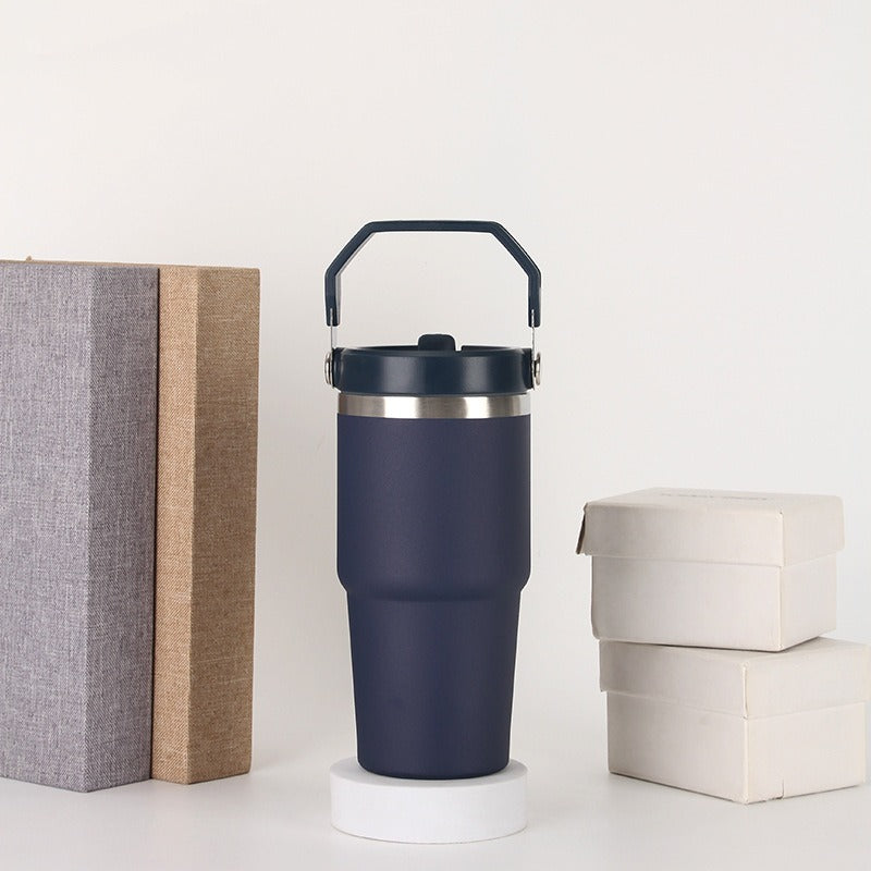 Navy insulated travel tumbler with handle, next to gift boxes and books, quality gifts