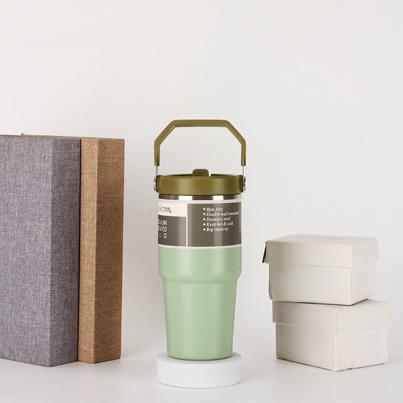 Green insulated stainless steel tumbler with handle, beside books and gift boxes on a white background