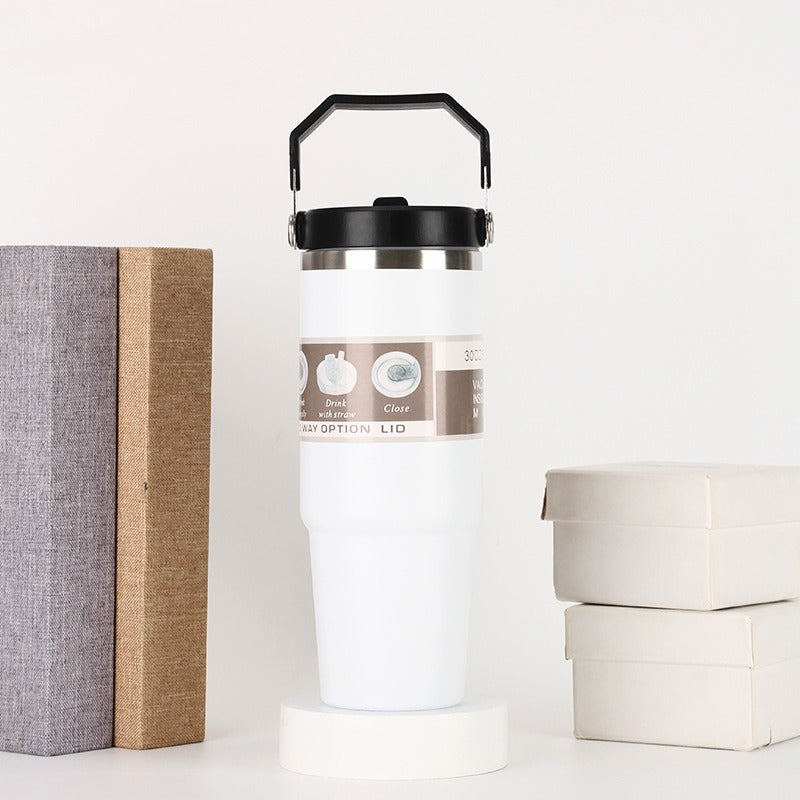 White insulated tumbler with black lid and handle, displayed beside books and gift boxes, quality gift item