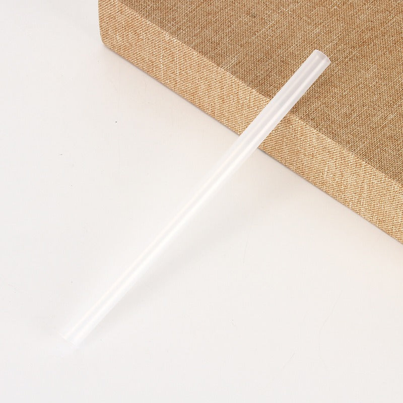 Clear reusable straw on white surface beside tan textured box, quality useful item